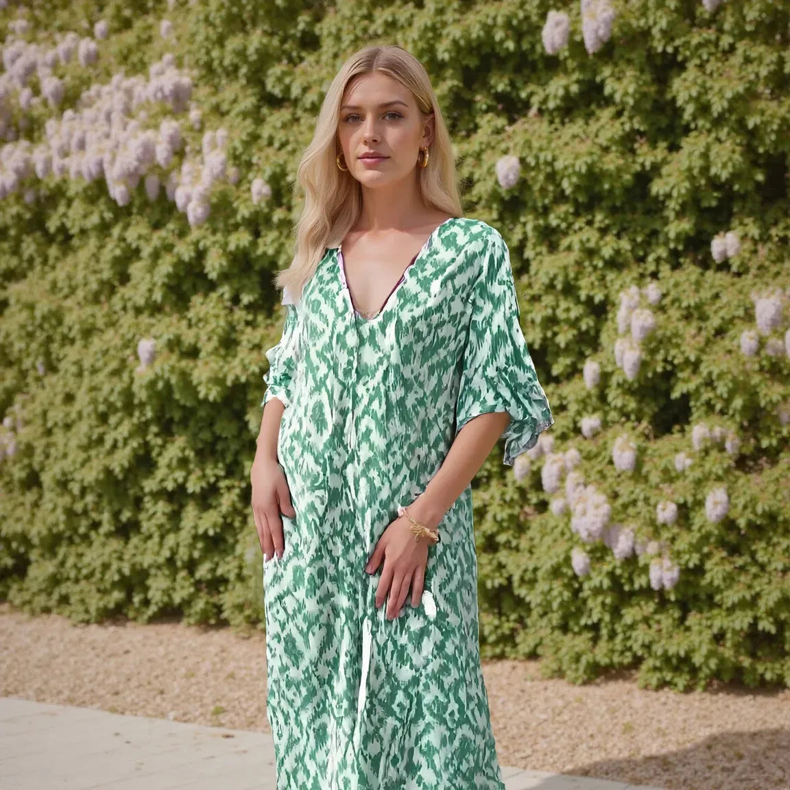 Woman wearing a green patterned dress standing in front of a bush with white flowers.