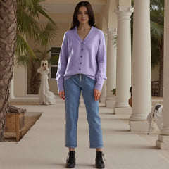 Woman wearing a purple cardigan and blue jeans standing in a palm tree-lined hallway.