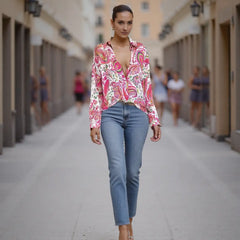 Woman walking down a street wearing a pink floral blouse and blue jeans.