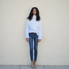 Person wearing a light blue sweater and dark blue jeans against a plain background