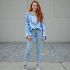 Woman wearing a blue patterned sweater and light blue jeans standing on a sidewalk.