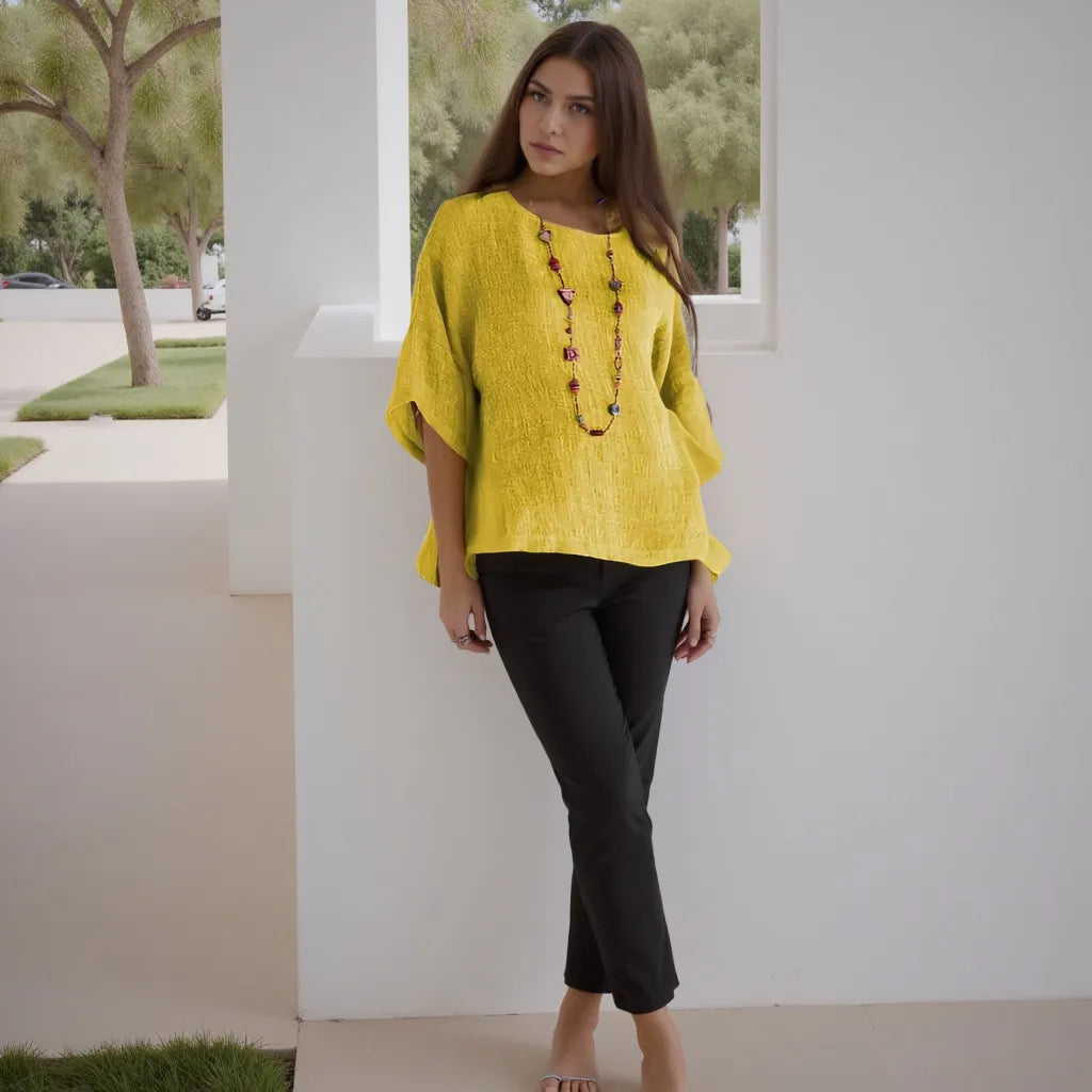 Woman wearing a yellow top and black pants standing in a modern outdoor setting.