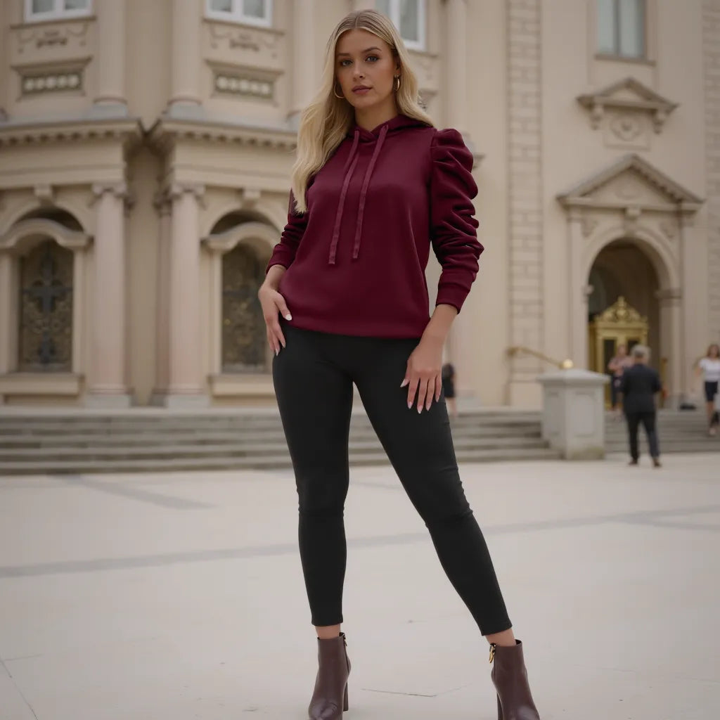 Woman wearing a burgundy hoodie and black pants standing in front of a building.
