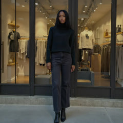 Woman in a black outfit standing in front of a clothing store with mannequins inside.