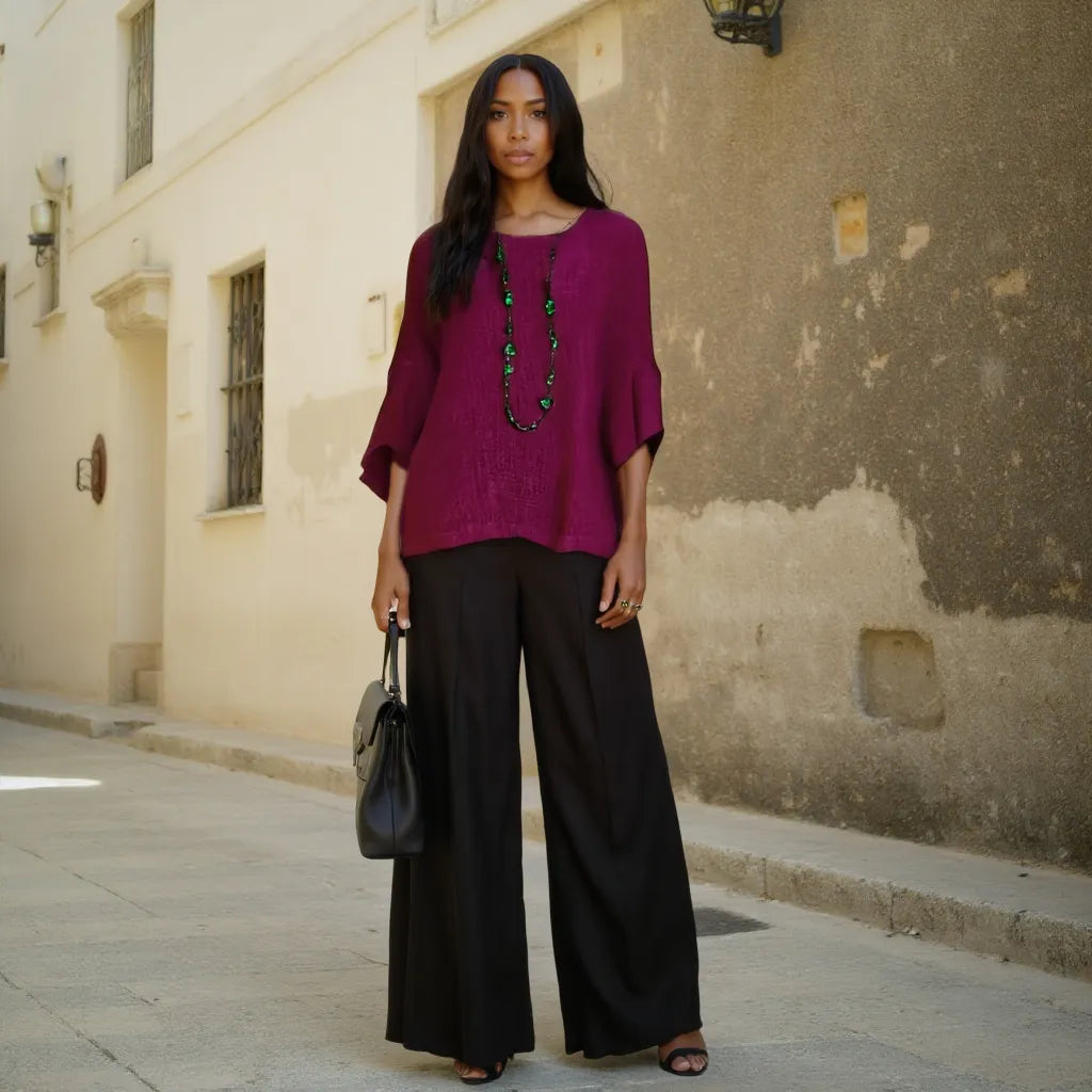 Woman in a purple top and black pants standing on a street.