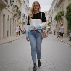Woman walking down a street wearing a black and white sweater with blue sleeves and light blue jeans.