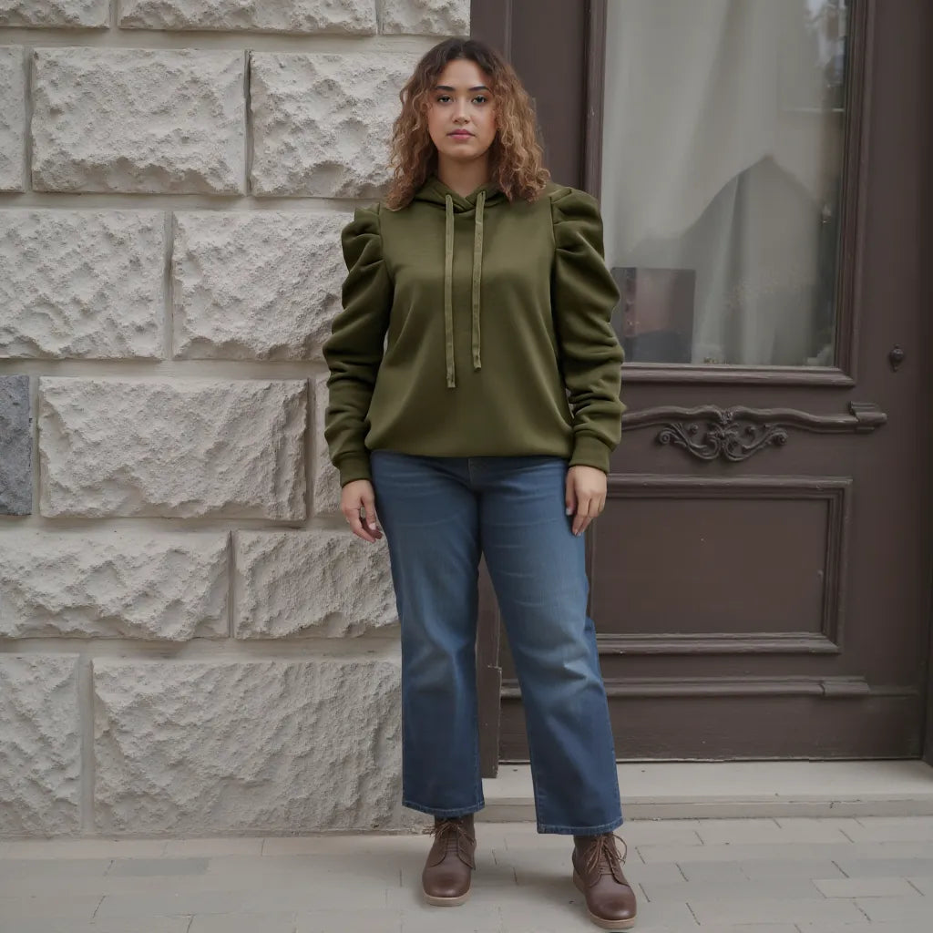 Woman wearing a green hoodie and blue jeans standing in front of a stone wall.