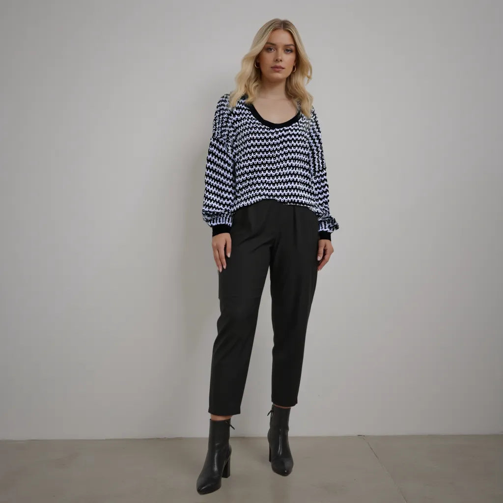Woman wearing a black and white patterned sweater with black pants against a plain background