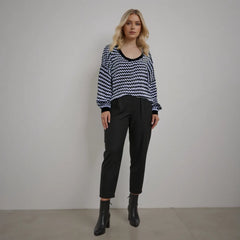 Woman wearing a black and white patterned sweater with black pants against a plain background