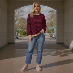 Woman wearing a red and black striped sweater and blue jeans standing under an archway.