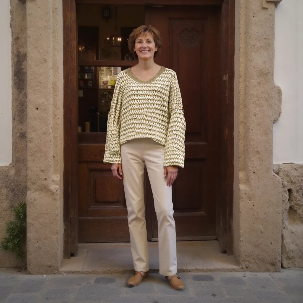 Woman standing in front of a wooden door wearing a light-colored sweater and beige pants.