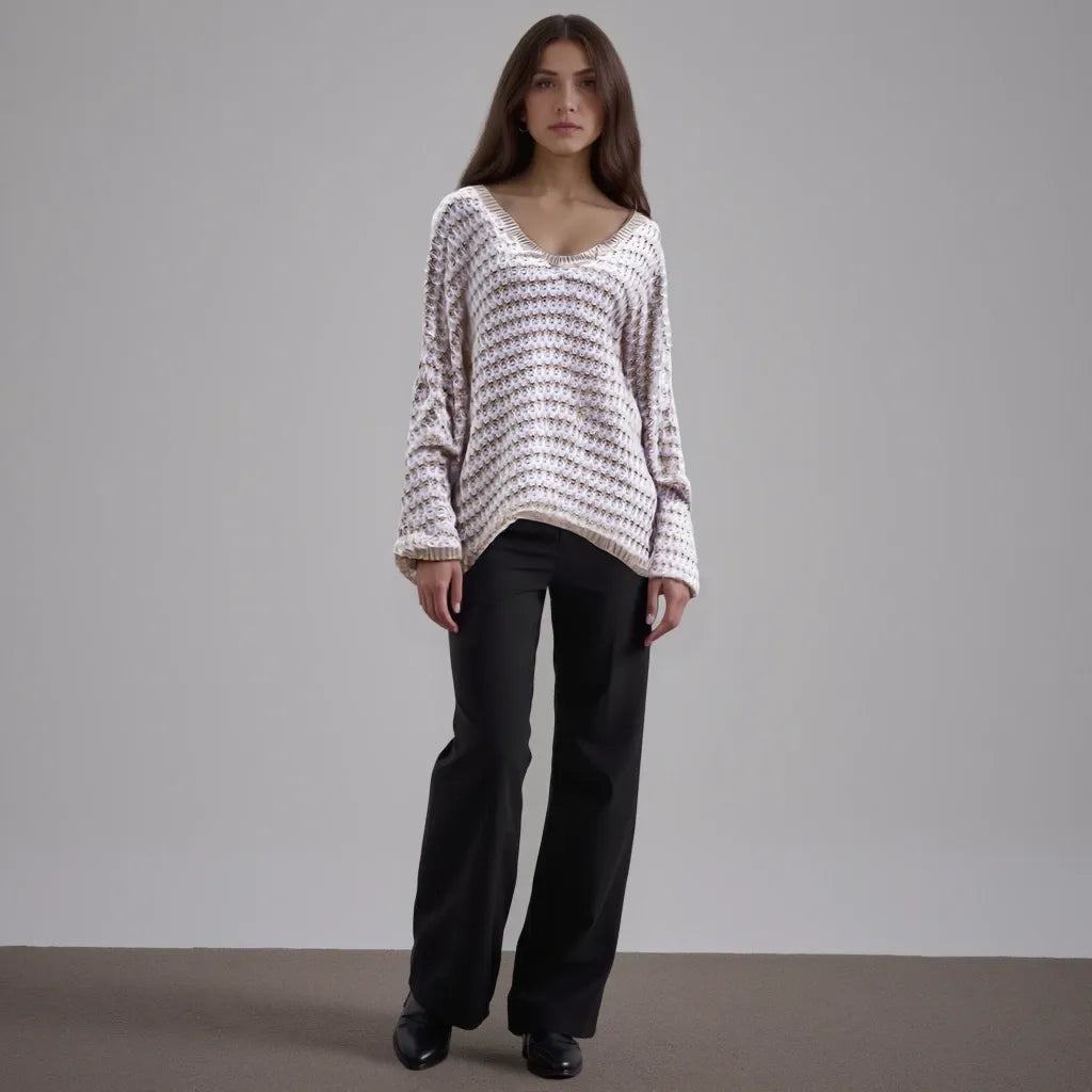 Woman wearing a patterned sweater and black pants against a plain background