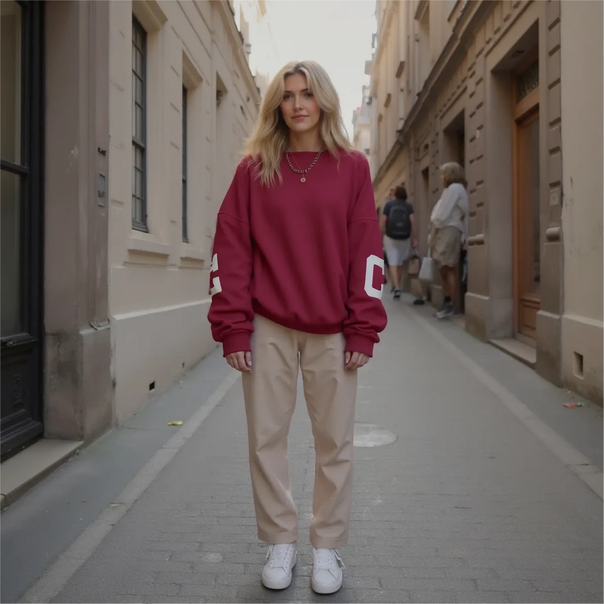 Woman wearing a red sweatshirt and beige pants standing on a city street.