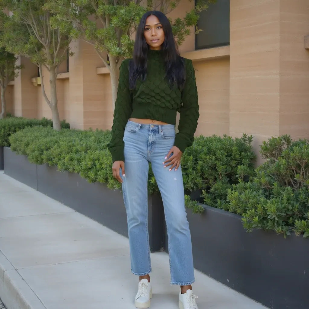 Woman in green sweater and blue jeans standing outdoors near a building