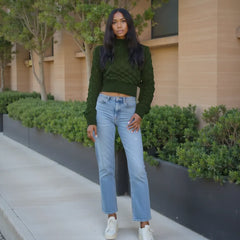 Woman in green sweater and blue jeans standing outdoors near a building