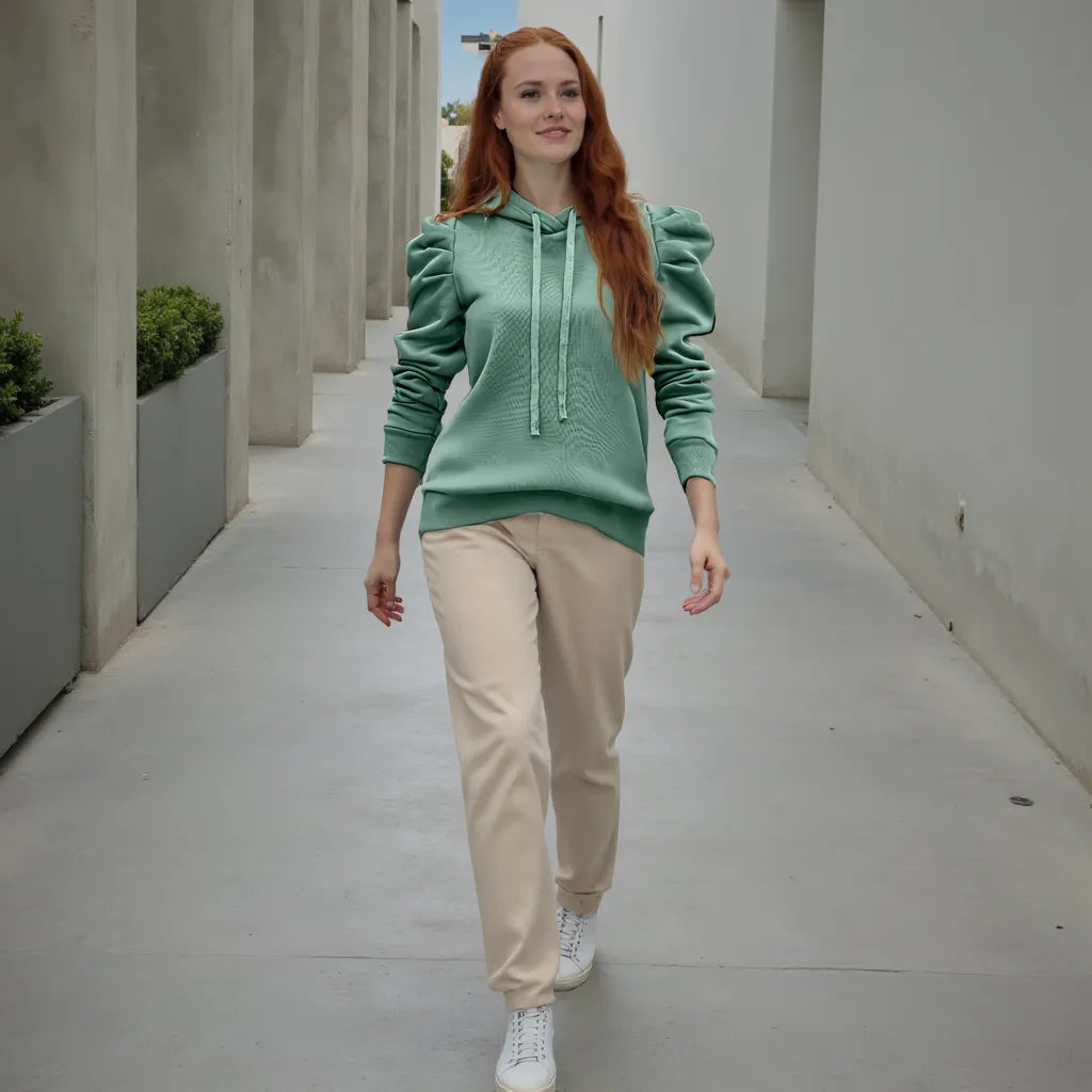 Woman in a green hoodie and beige pants walking in an outdoor setting.