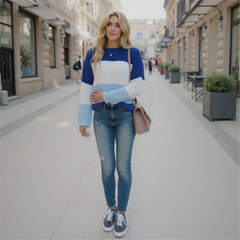 Woman wearing a blue and white sweater with jeans on a city street.