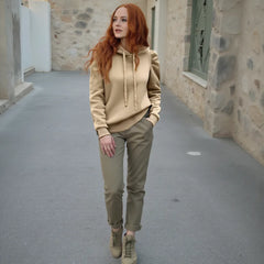 Woman walking in a narrow alleyway wearing a beige hoodie and green pants.