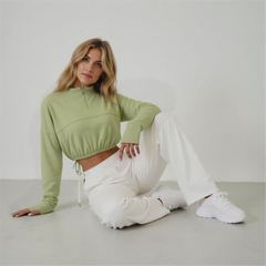 Woman wearing a green top and white pants sitting on a light gray floor.