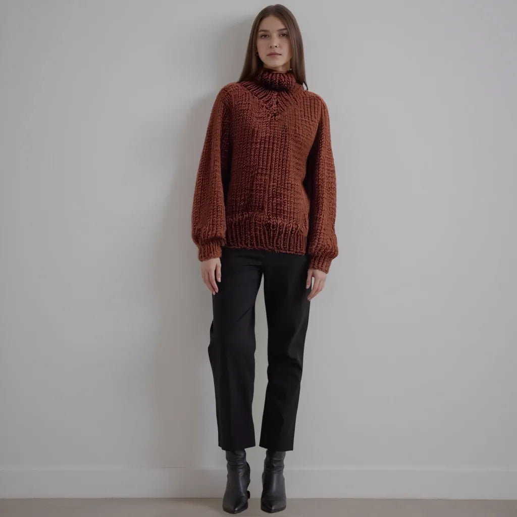 Woman wearing a brown knitted sweater and black pants against a plain background