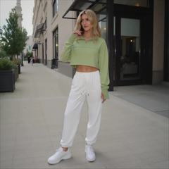 Woman in a green crop top and white pants standing on a city street.