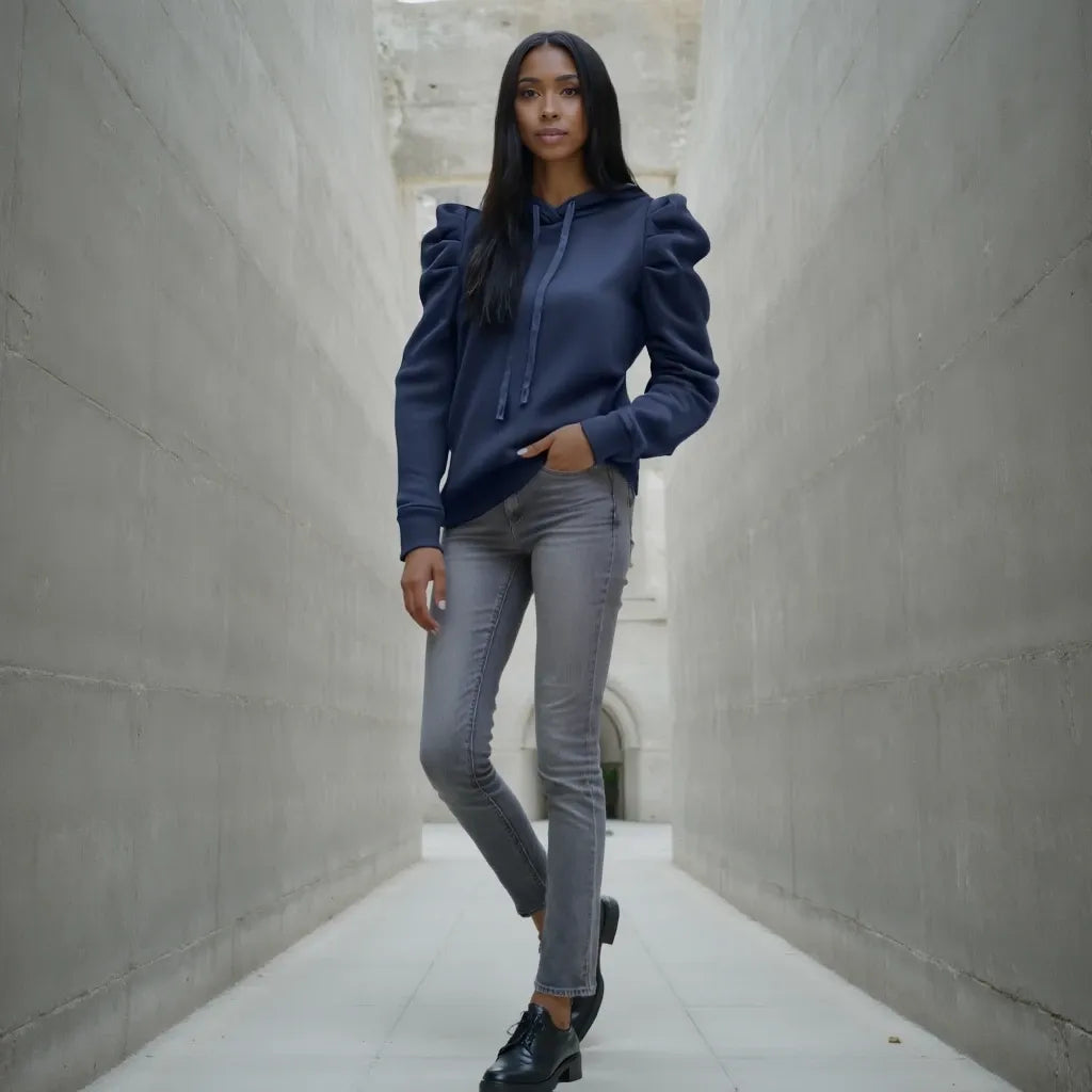 Woman wearing a navy blue hoodie and gray jeans standing in a narrow alleyway.