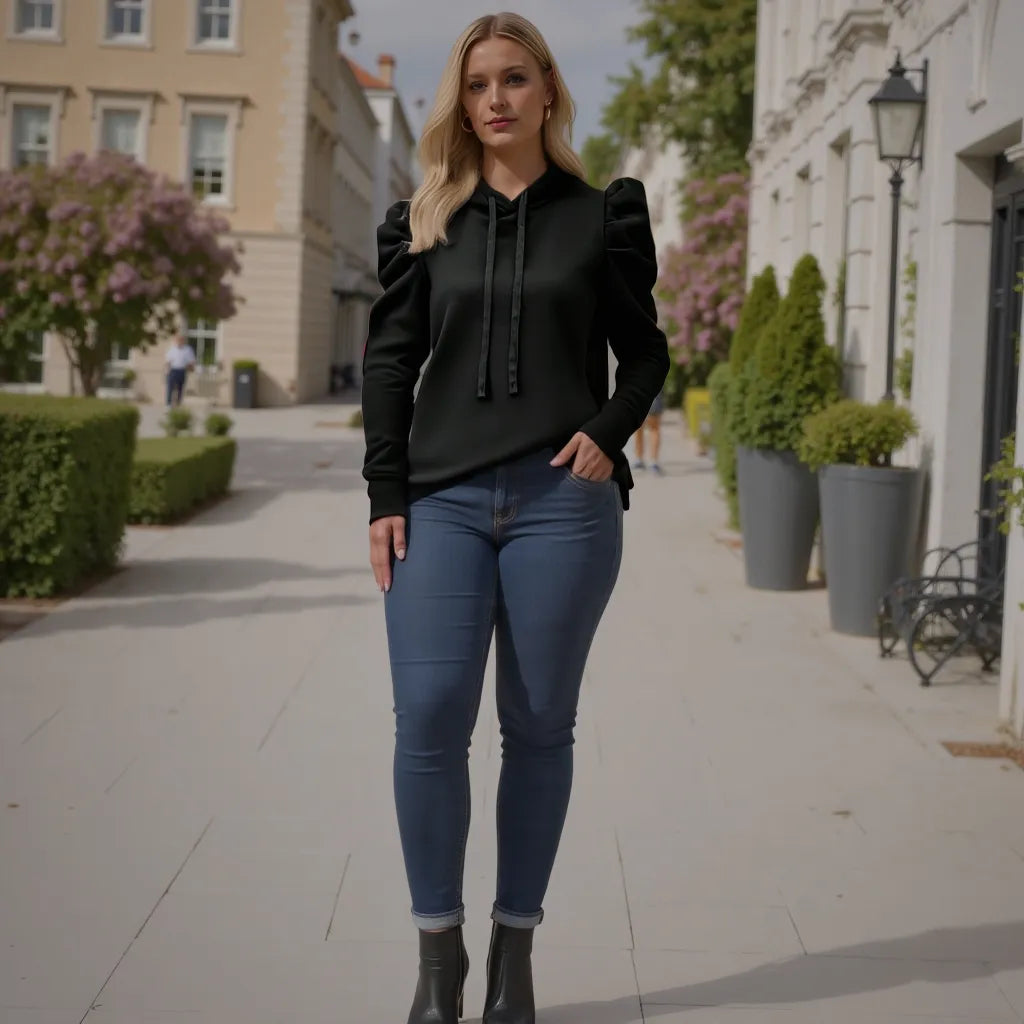 Woman in black hoodie and blue jeans standing on a city street.