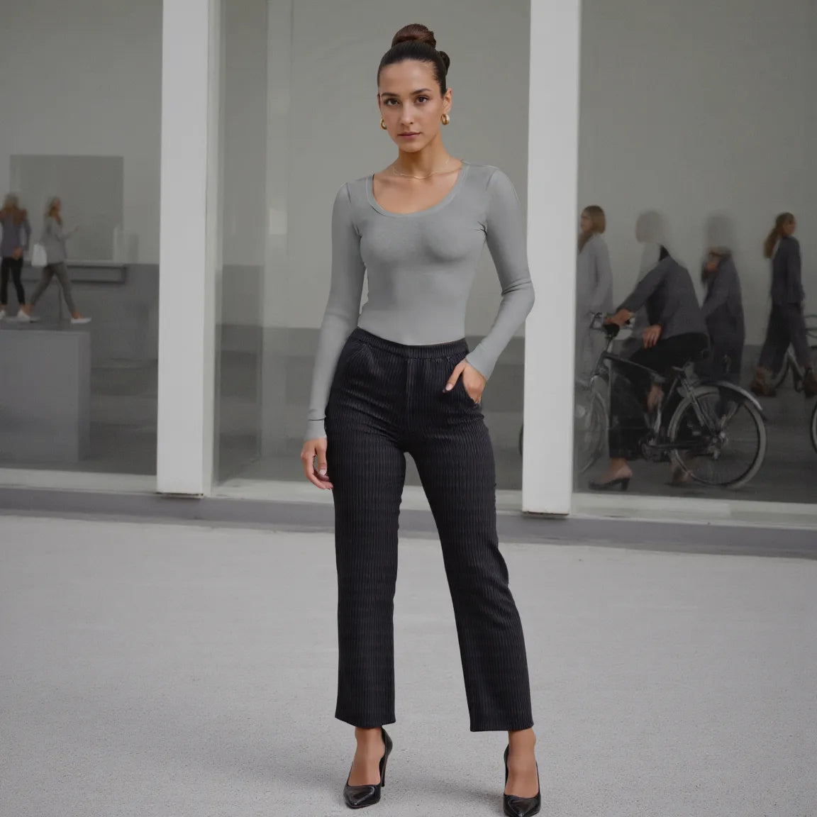 Woman in gray long-sleeve top and black pants standing in a modern indoor setting.