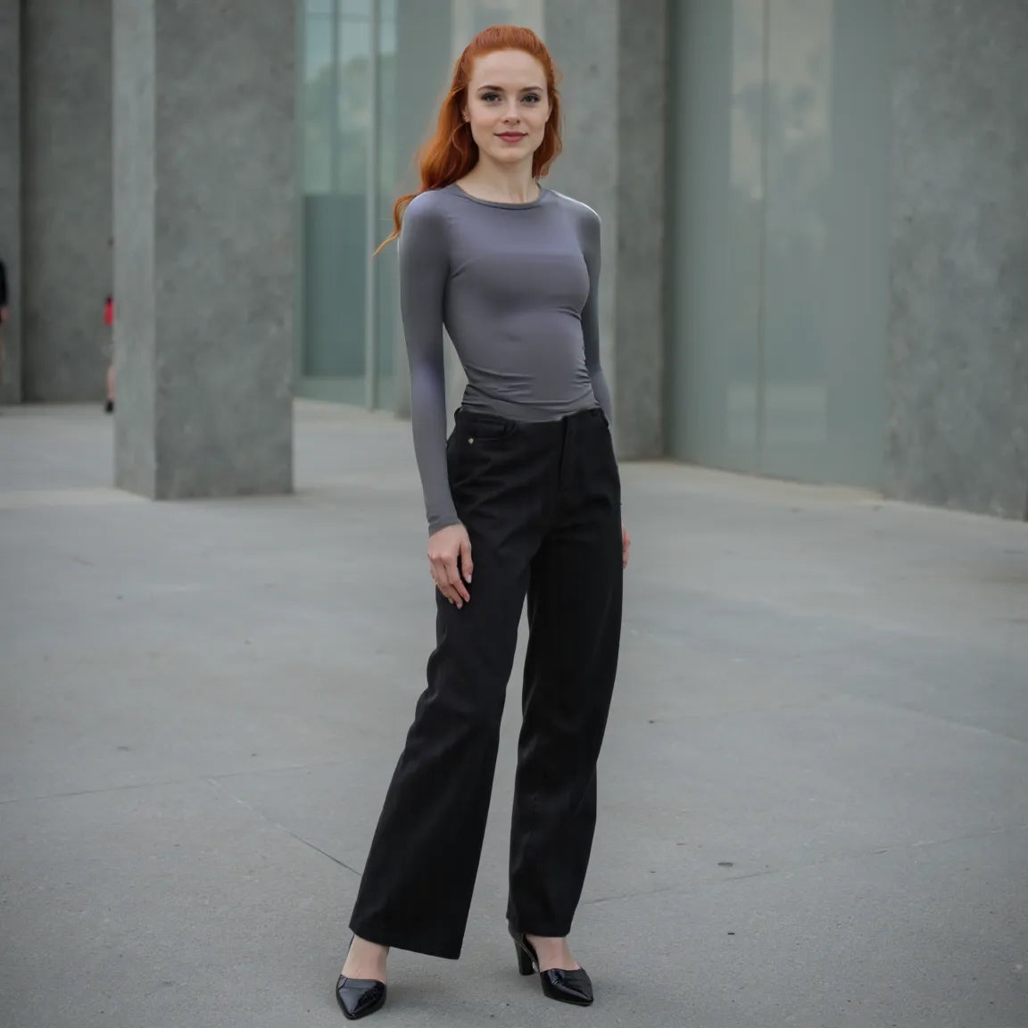 Woman wearing a gray top and black pants standing in an urban setting.