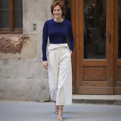 Woman in a blue top and white pants standing in front of a building entrance.