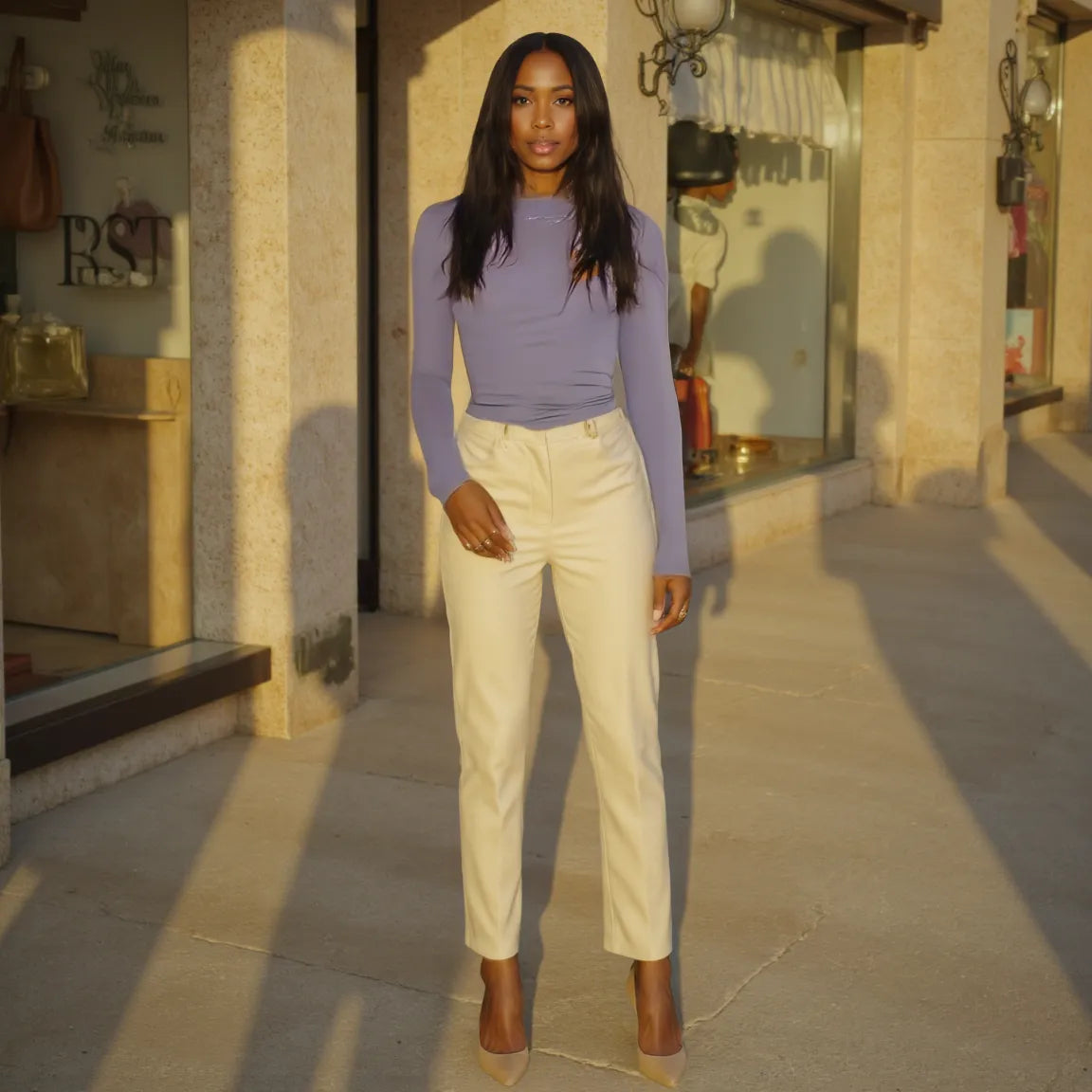Woman in a purple top and white pants standing on a stone pavement.