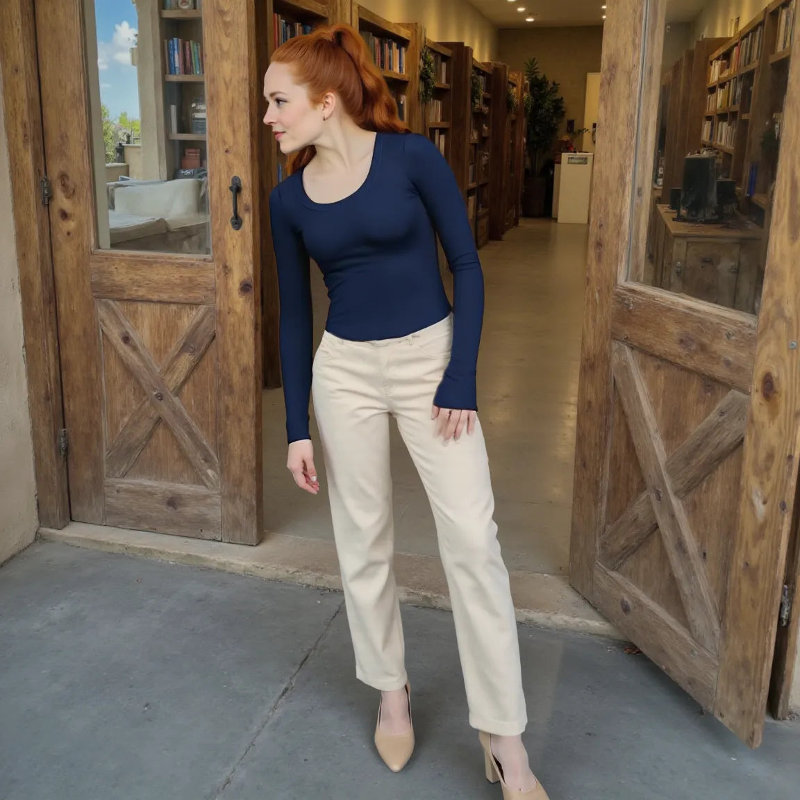 Woman in a blue top and beige pants standing in a room with wooden doors and bookshelves.