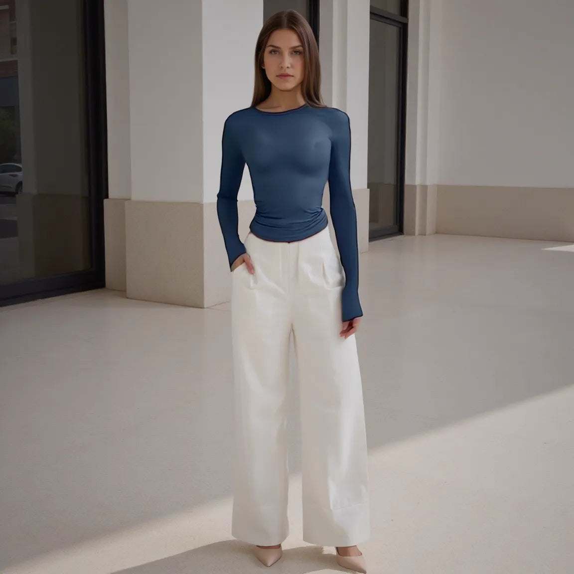 Woman wearing a blue long-sleeve top and white pants in a minimalistic setting
