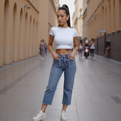 Woman in a white crop top and blue jeans walking on a city street.