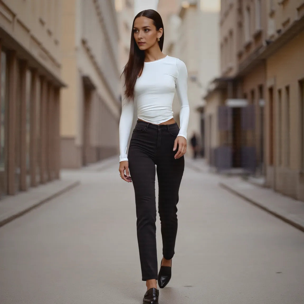 Woman walking down a city street wearing a white top and black pants.
